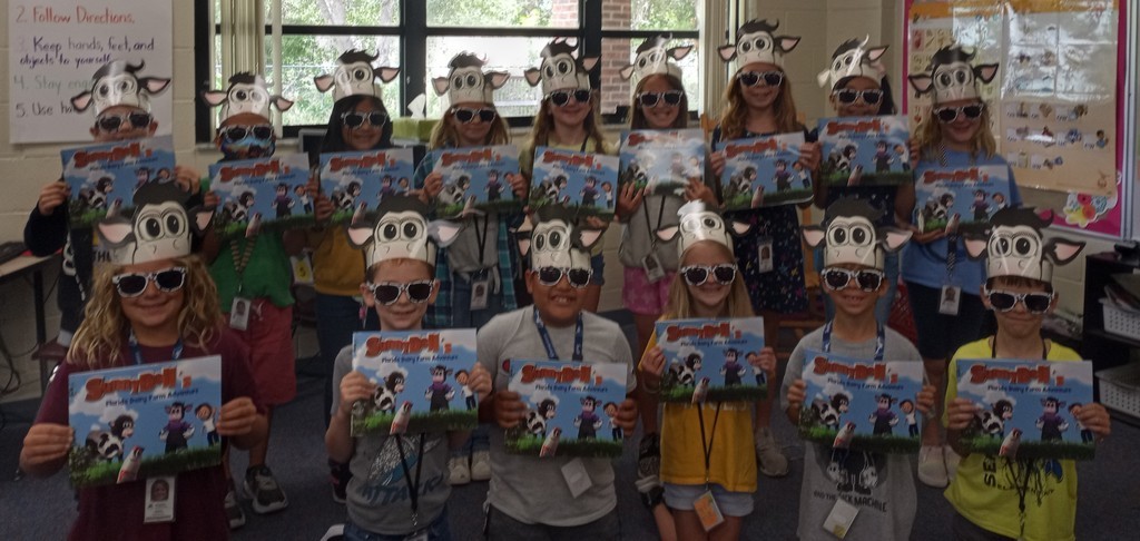 Students wearing silly cow hats showing off their picture books. 